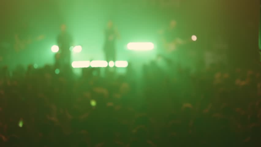 Energetic crowd cheering and applauding band on stage with colorful lighting
