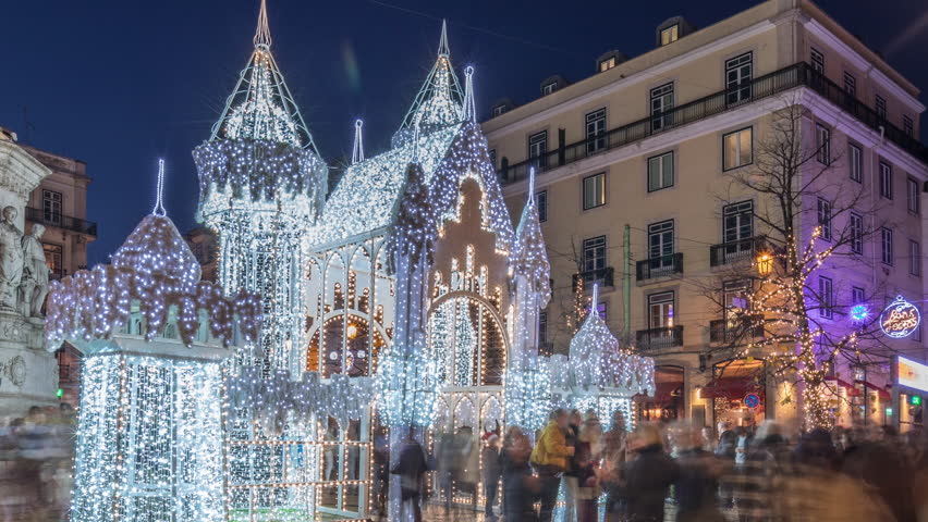 Night timelapse hyperlapse of Christmas decorations with illuminated castle on Luis de Camoes square in Lisbon, Portugal. People walking around the festive lights and historic architecture. Front view