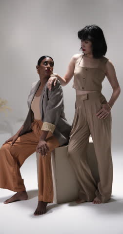 Vertical video: Two women in stylish outfits posing confidently in modern fashion studio. style, elegance, confidence, trend, contemporary, couture