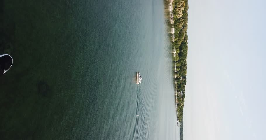 4K vertical aerial drone video of a white boat floating across the water from right to left in Lake Geneva, Wisconsin.