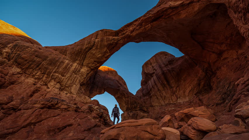 Cinemagraph time-lapse of young man watching golden sunrise at sandstone Double Arch in Arches National Park, Utah, USA