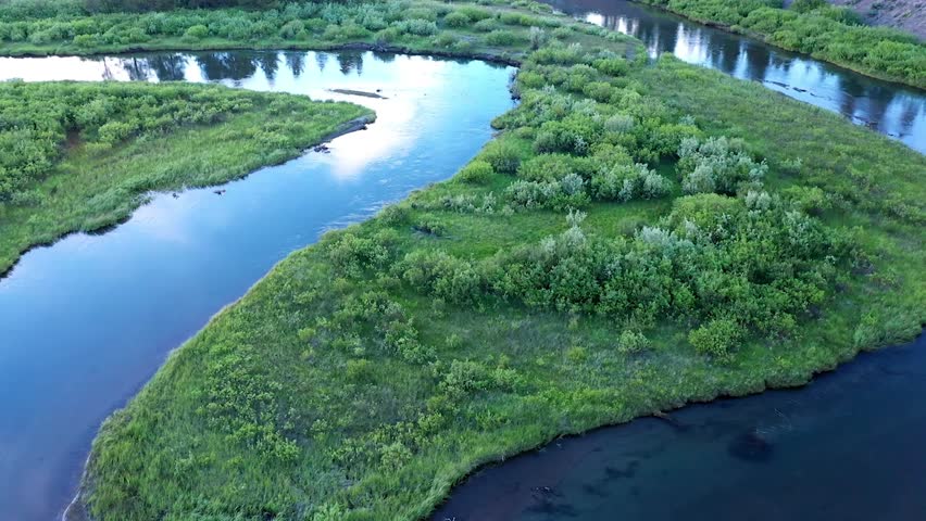 View of river winding through green meadow in Montana while rising in aerial view.