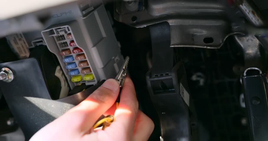 Close-up footage of a person testing a car fuse box with a voltage tester, highlighting vehicle maintenance and electrical diagnostics inside a vehicle's dashboard area