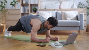 Young asian man doing plank exercise in living room at home while watching online workout tutorial on laptop with endurance and motivation, man training plank on yoga mat, digital fitness lifestyle. - Powered by Shutterstock - Get 15% off with code: PIKWIZARD15