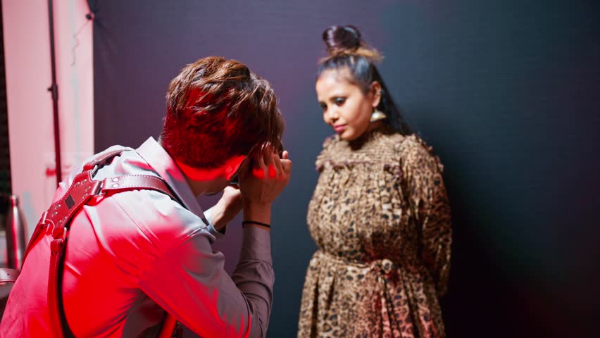Cameraman records bold talent inside photo venue, Model wears wild pattern outfit with flair in studio, Photographer lead woman through lively stance, Modeling shoots with vivid brightness setup, Icon