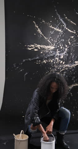 Vertical video: Artist creating abstract splatter painting on black wall in creative studio. creativity, artistic, contemporary, expression, design, modern