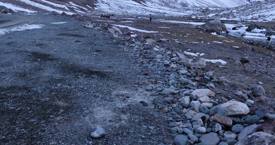 Sacred Gumbo Ronjon mountain in Zanskar Valley, Ladakh, with melting stream and snow-covered winter landscape under cloudy sky