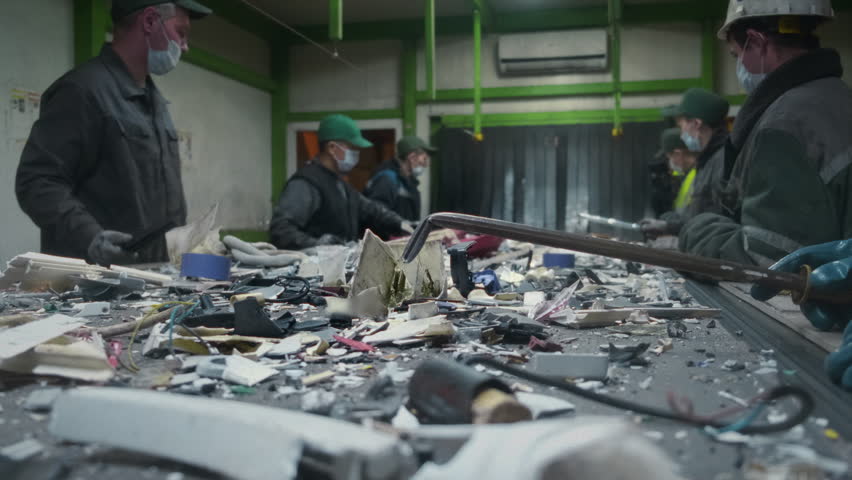 Men workers of garbage processing plant sort garbage. Male workers sort and recycle scrap metal. Plastic, polymer household waste is transported on conveyor belt in factory. Ecology of planet. Man