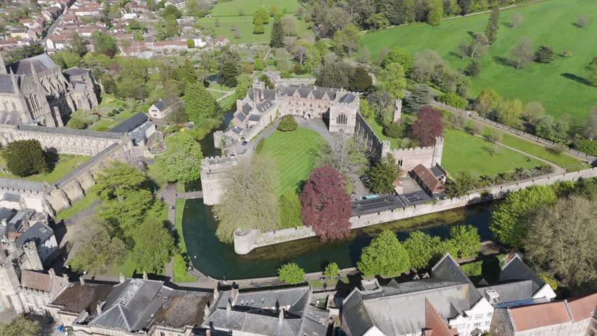 Aerial orbit of medieval palace complex with stone towers, moat and formal lawns, highlighting historic architecture and tranquil green surroundings for heritage storytelling