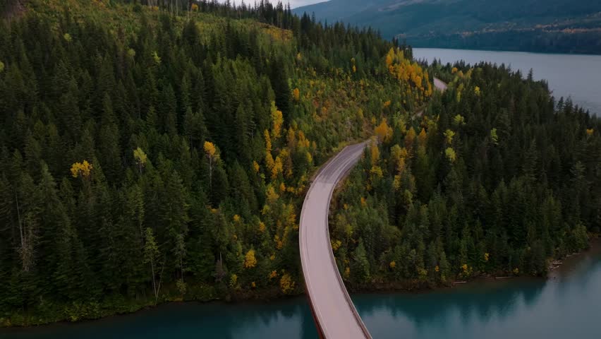 Beautiful drone shot of car driving through mountains and lake with fall colours