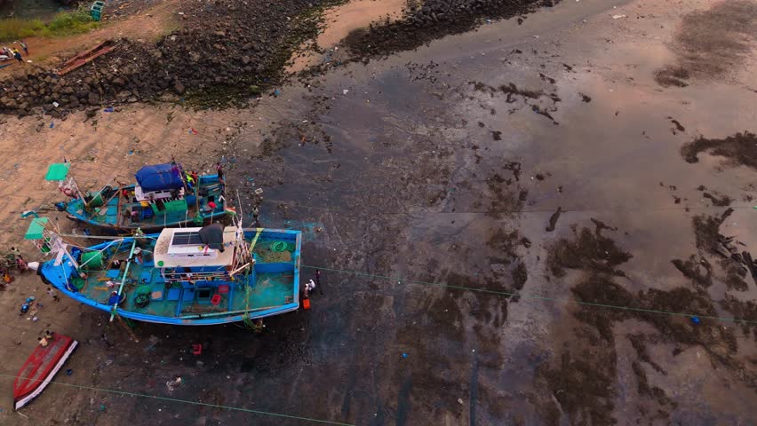 Aerial View of Fishing Boats on a Sandy Beach, Drone Capture Lively Vessels and Coastal Waste, Tourists Roam Along Shoreline Strewn with Debris, Colorful Marine Fleet Anchors at Rugged Waterfront