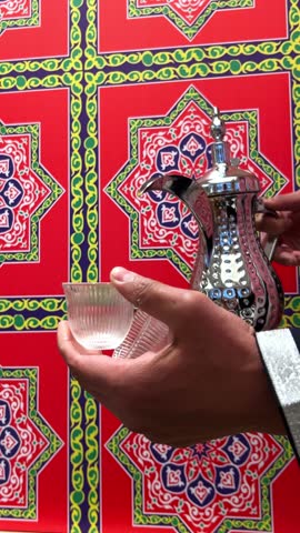 4K close-up of Arabic coffee being served in a traditional dallah pot with a vibrant Islamic-pattern background. Ideal for Ramadan, hospitality, or Middle Eastern culture visuals.