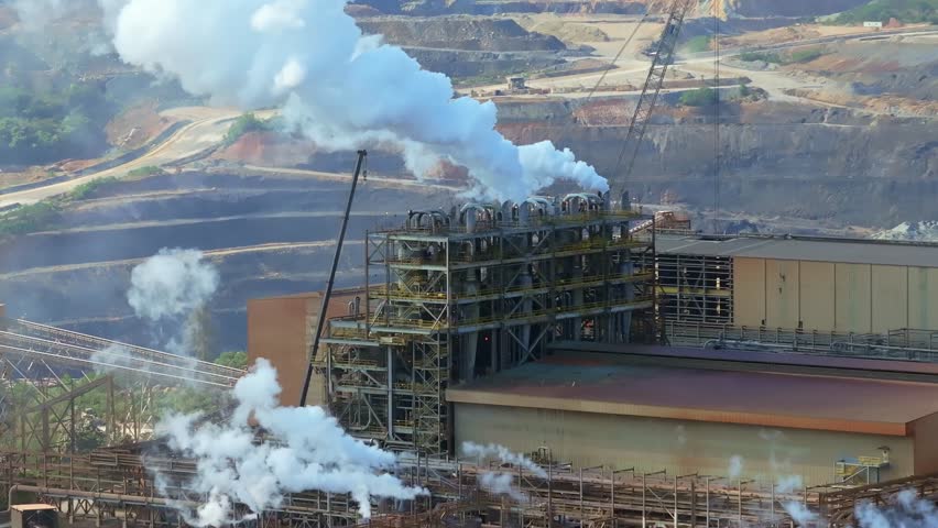 Barrick Gold mining facility with metal structures release large plumes of steam near terraced open pit mine in Cotuí, Dominican Republic. Aerial view