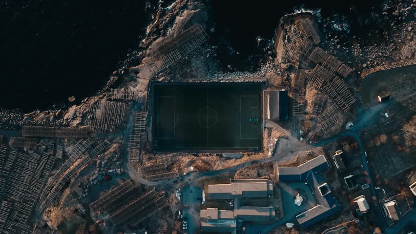 Top View Of Soccer Field At Reine Stadion Surrounded By Rugged Terrain And Coastal Waters In Reine, Norway. aerial shot
