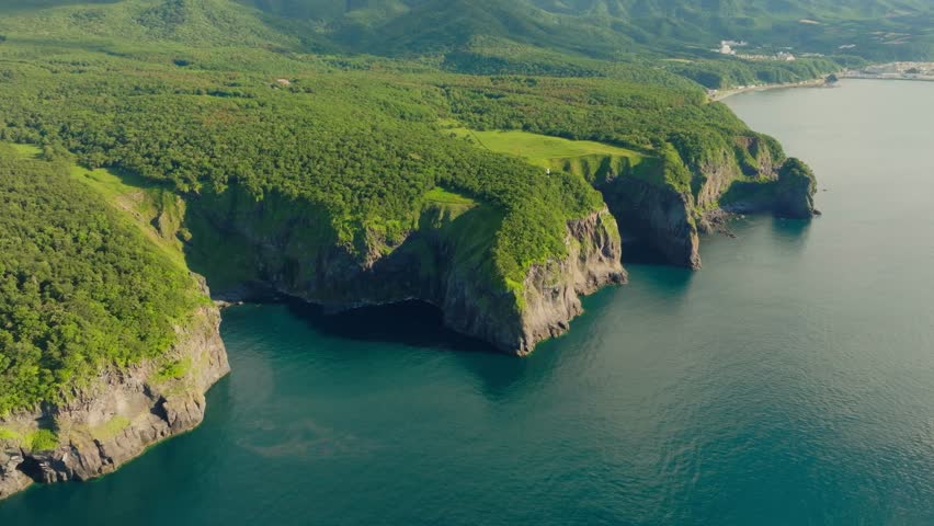 Aerial fly above waters and green rocky coast in Shiretoko Peninsula, Hokkaido, Unesco National Park