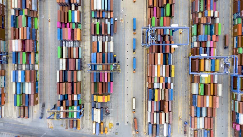 Aerial overhead hyper lapse view of a industrial cargo container port with loading and unloading activity of ships by trucks and cranes