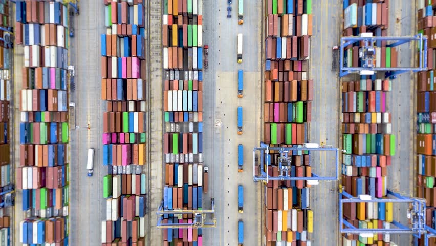 Aerial overhead hyper lapse view of a industrial cargo container port with loading and unloading activity of ships by trucks and cranes