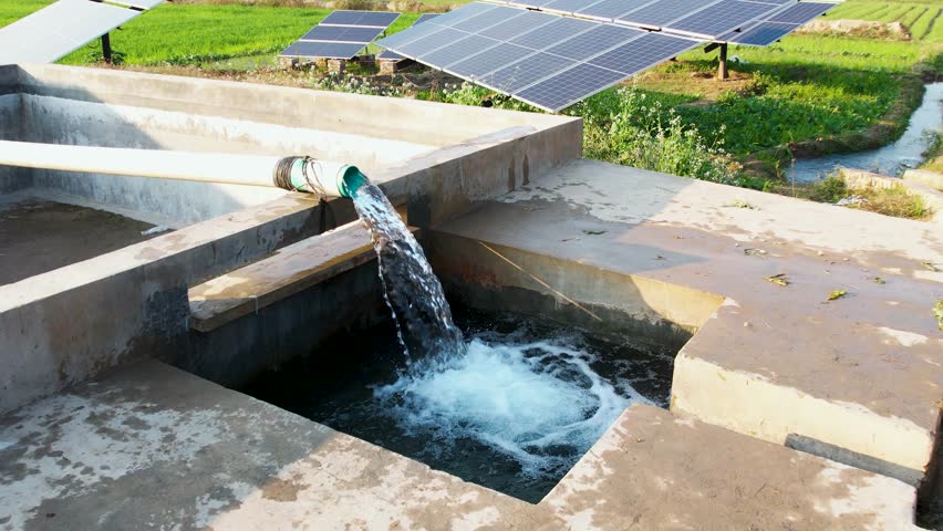 Water flows from a solar-powered tubewell beside solar panels used for irrigating nearby farmland. Punjab, Pakistan