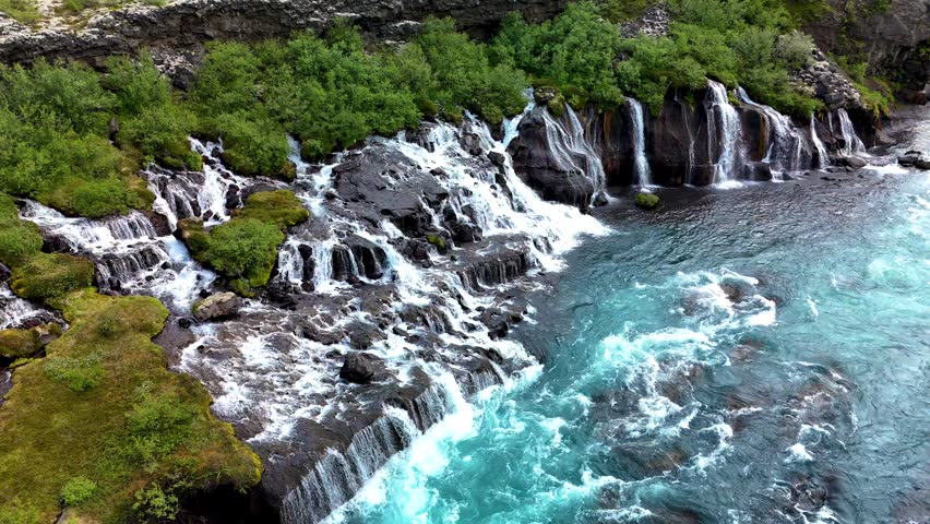 Majestic Barnafoss and Hraunfossar waterfalls cascade over rugged lava rocks, creating a stunning display of turquoise waters surrounded by lush greenery.