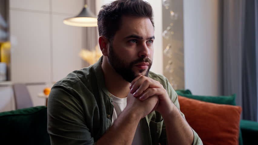 Nervous thoughtful Caucasian business man male guy client homeowner businessman sitting sofa folded hands think deep difficult thoughts stress decision burnout mental health problems home living room