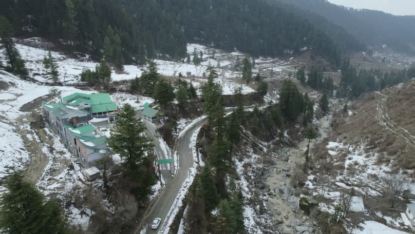 A long road with cars driving between mountains covered in greenery and snow in Bhaderwah, Jammu and Kashmir, India.