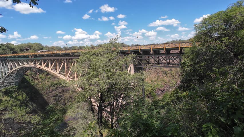 The Victoria Falls Bridge surrounded by vegetations and clear blue sky with scattered white clouds in Zimbabwe