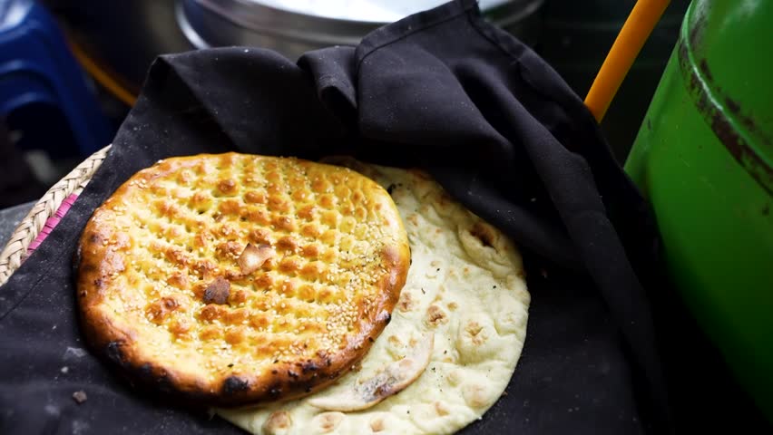 A hand places soft roti atop a baked naan in a traditional tandoor setup. Azerbaijan