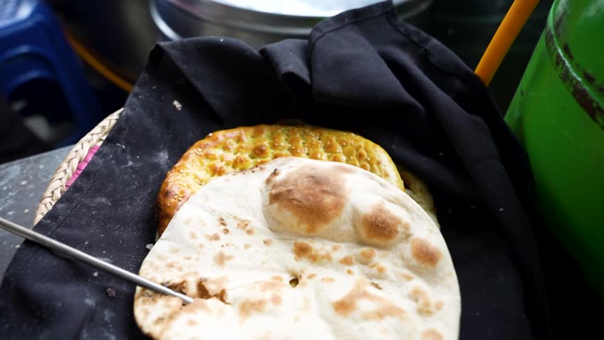 A hand places soft roti atop a baked naan in a traditional tandoor setup. Azerbaijan