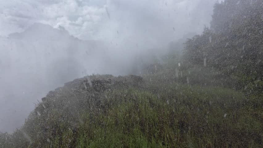 A misty atmosphere around Victoria Falls with powerful stream and steam under cloudy sky in Zimbabwe