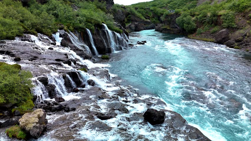 Discover the enchanting Barnafoss and Hraunfossar waterfalls, where clear turquoise waters flow gracefully over rugged rocks. A serene journey through Icelands natural beauty awaits.