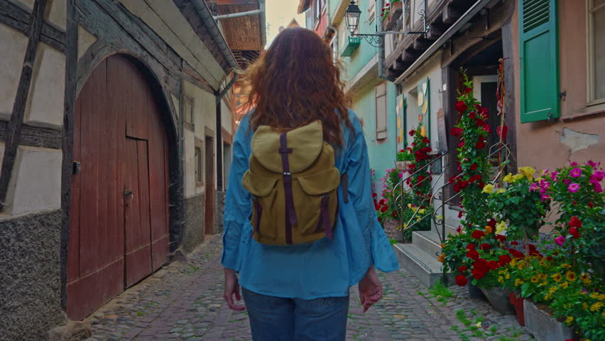 Woman with backpack walking on the beautiful street full of colorful houses with flowers of Eguisheim, France 