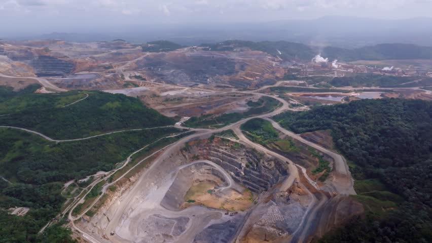 Drone footage showcases the immense scale of Barrick Gold Pueblo Viejo open-pit mine, with terraced excavation and distant processing plant. Overcast. Dominican Republic