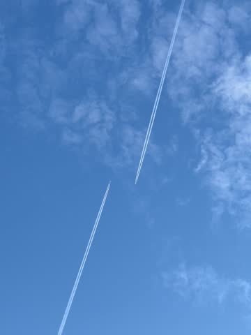 Two airplanes flying high in the clear blue sky, leave long white contrails behind them in a striking aerial scene