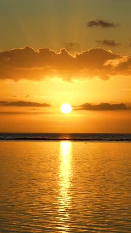 Slow motion of a breathtaking golden sunset over the tranquil ocean, with a bright sun reflecting on the water and clouds in the sky