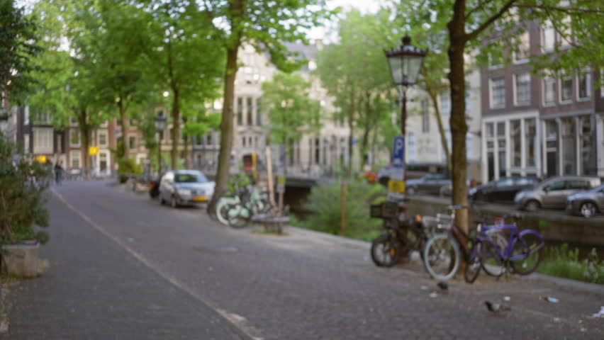 Blurred image of amsterdam street with bicycles, trees, and canal, showcasing urban life and architecture in the netherlands.