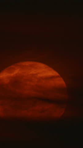 close-up of a blood moon glowing in deep orange hues, partially veiled by wisps of dark clouds. This atmospheric celestial scene captures the mysterious and dramatic beauty of the lunar surface.
