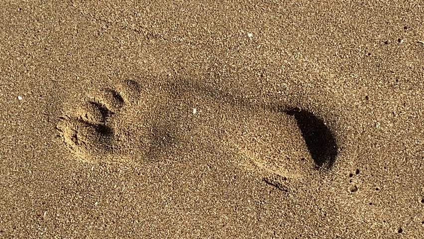A close-up of a human footprint in soft beach sand as it