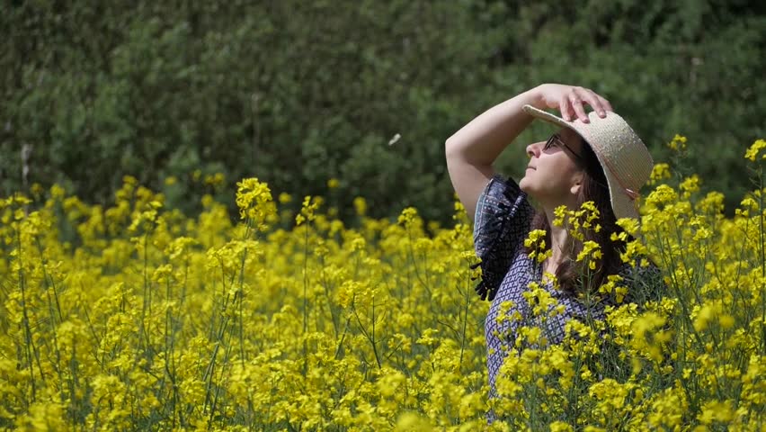 butterfly flutters slow motion in dreamy rural landscape, woman enjoys sun in rapeseed field