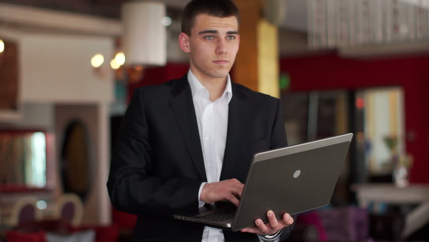 Young man standing in a cafe with a laptop and laughing
