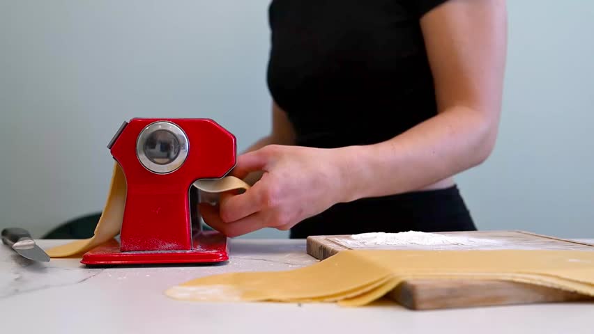 Traditional pasta-making close-up: a woman uses a hand-crank roller to flatten fresh dough into thin sheets. minimalist video