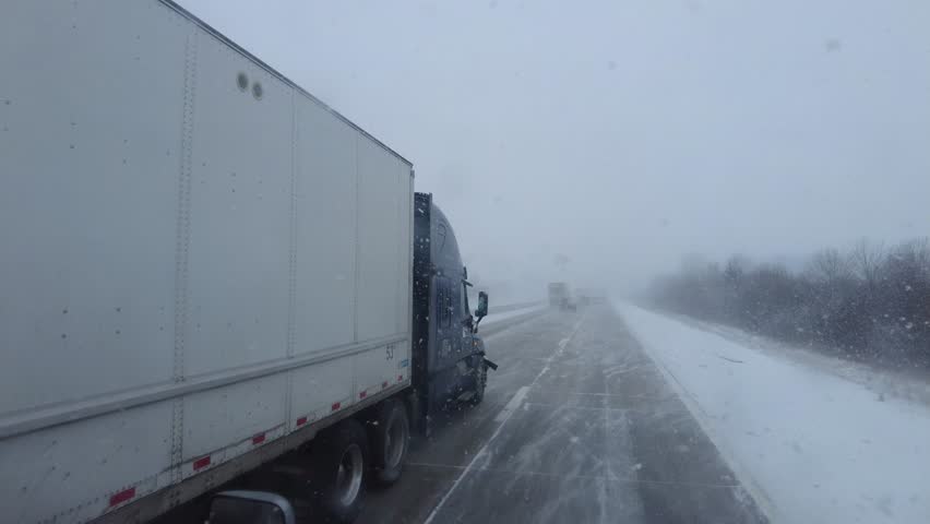 Freight trucks and passenger cars crawl through the snow-covered I-80 in Ohio. A fierce snowstorm and low visibility make the road nearly impassable as ice builds up on the interstate surface.