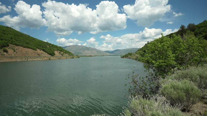 Static shot of calm water at Pineview Lake in Utah, surrounded by early summer greenery and distant hills. Peaceful nature scene captured with a tripod.