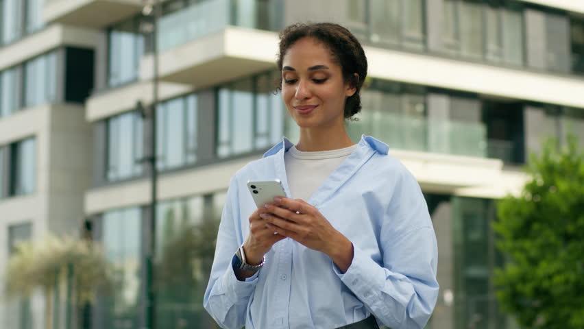Satisfied African American woman female girl worker businesswoman business lady user holding mobile phone order taxi shopping online internet app smartphone in city outdoors looking at camera smiling