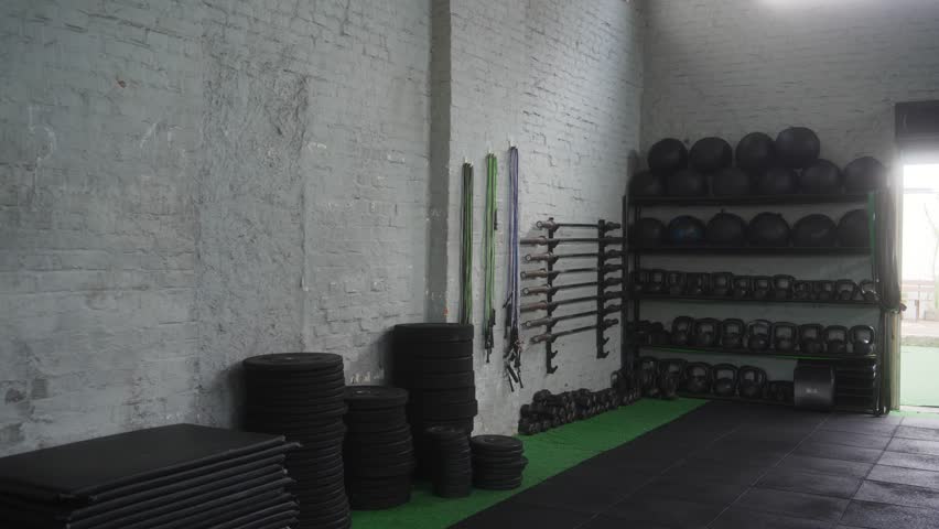Mid adult athletic man selecting jump rope from equipment wall in modern functional training gym with white brick interior preparing for intense cardio workout routine