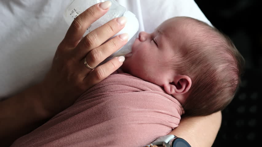 Mother Feeds Newborn Baby Formula From A Bottle As The Infant Consumes Milk Formula
