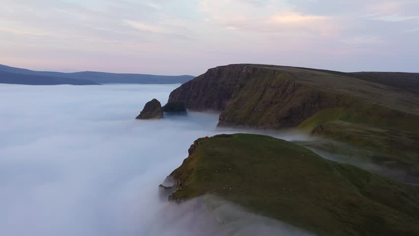 Campers in tents, camping above the clouds at sunrise on the Quiraing Isle of Skye, Scotland - Mountains piercing though the clouds as the sun rises over the horizon 