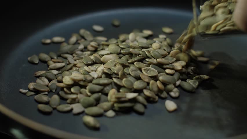 This is a detailed closeup sequence that showcases the process of toasting raw pumpkin seeds in a skillet, effectively demonstrating how to prepare delicious and healthy ingredient for various dishes