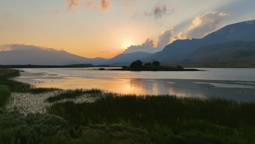 Drone shot of a lake surrounded by mountains at sunset