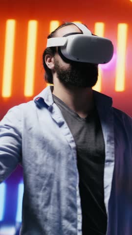 Vertical Video Cool modern guy showcasing artistic vibes with his virtual reality glasses, surrounded by colorful neon lights in a cyberpunk atmosphere for entertainment. Nightlife minimalism. Camera