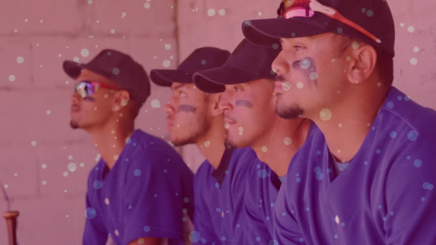 Opening shot showing baseball players in dugout facing field watching game under floating specks. Athletes, team spirit, sportswear, competition, concentration, camaraderie, outdoor